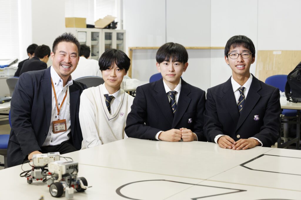 メカニカルアーツ部の部室にて撮影。左から、大澤教諭、「meiden1年チーム」の猪俣くん、楠本くん、堀田くん。